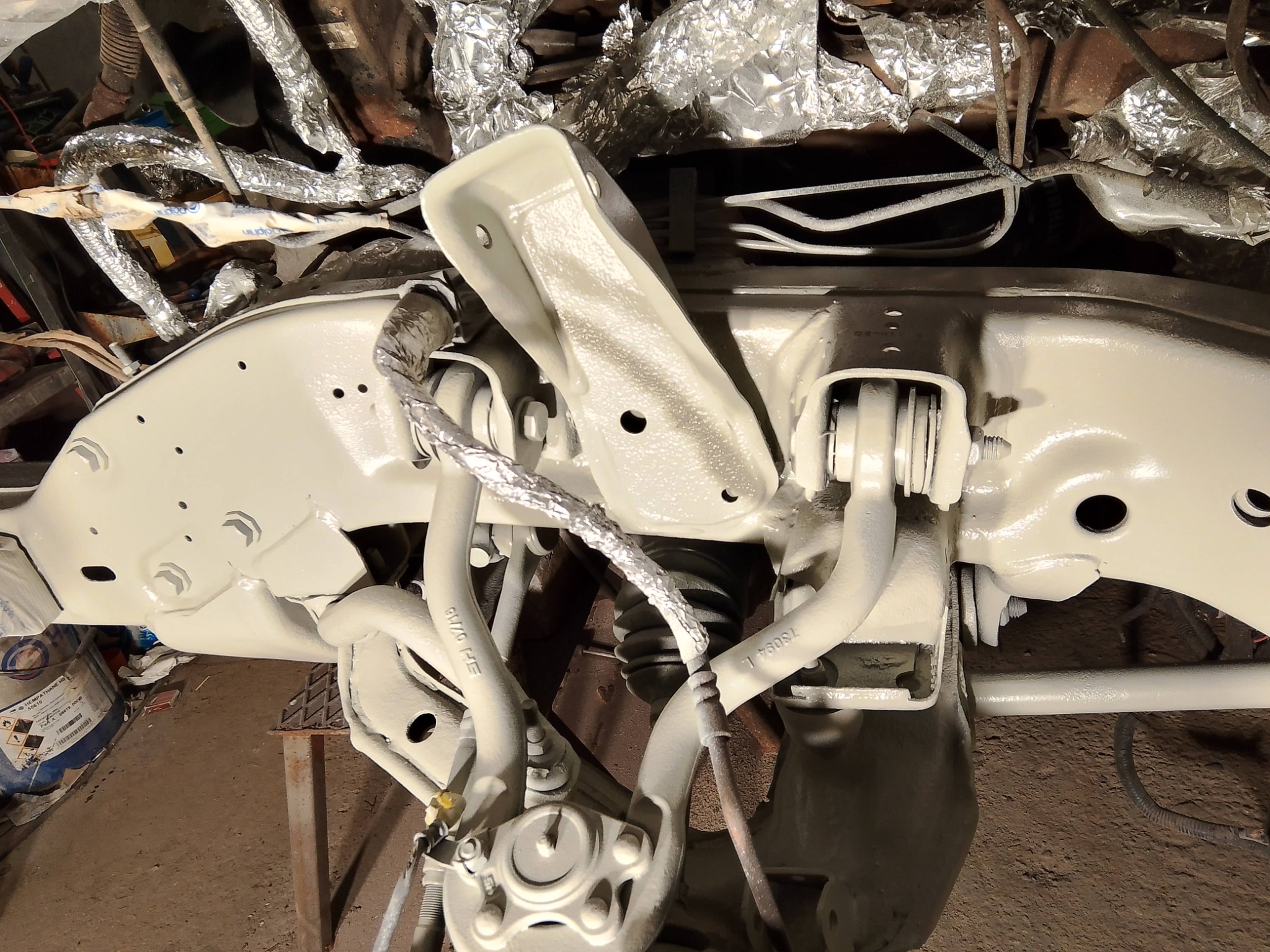 Zawieszenie pojazdu po piaskowaniu i nałożeniu farby antykorozyjnej, widoczne elementy owinięte folią ochronną, detale konstrukcyjne i przewody.