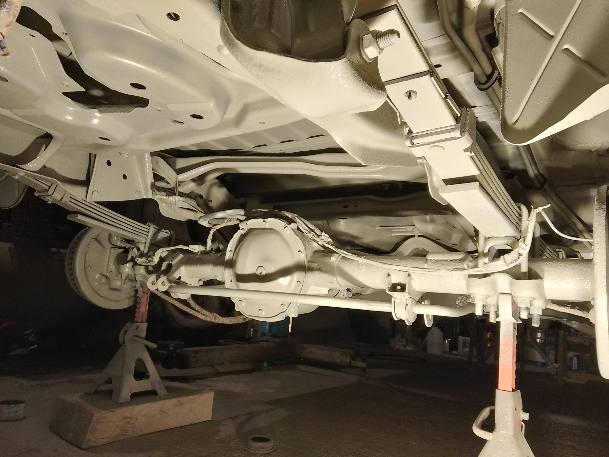 Podwozie samochodu po zabezpieczeniu antykorozyjnym, pomalowane na biało, wsparte na podnośnikach warsztatowych. Widoczne elementy zawieszenia i układu napędowego.