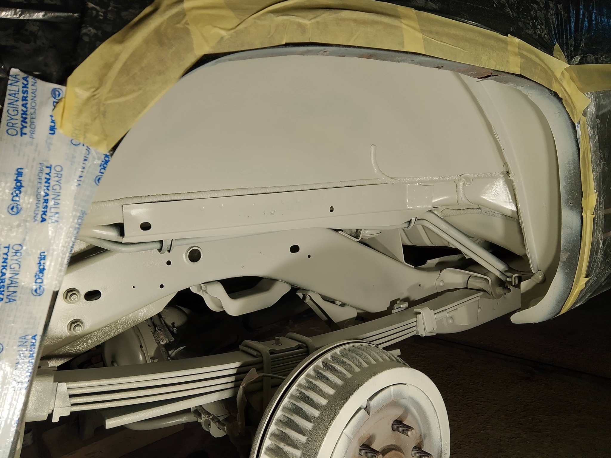 Podwozie samochodu po piaskowaniu i zabezpieczeniu antykorozyjnym, przygotowane do dalszych prac. Widoczne elementy zawieszenia i koła pokryte farbą.