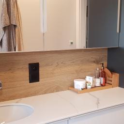 REMIS-AVS sp. z o. o. - Nowoczesna łazienka z drewnianą okładziną ścienną, białą umywalką Villeroy & Boch i blatem z białego marmuru, uzupełniona o czarny dozownik mydła i chromowaną armaturę.