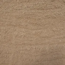 Beżowy, drobnoziarnisty materiał sypki z widocznymi śladami po przesuwaniu, prawdopodobnie piasek budowlany.