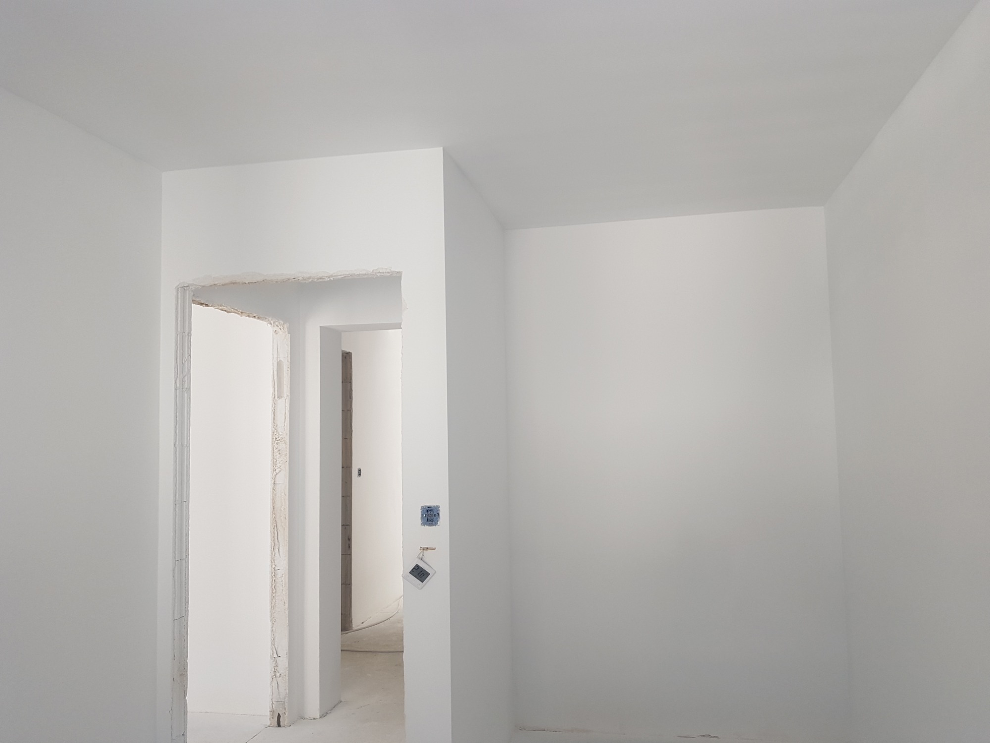 Wnętrze po remoncie, ściany i sufit pomalowane na biało, widoczne gniazdka elektryczne i ościeżnica drzwiowa przed wykończeniem.