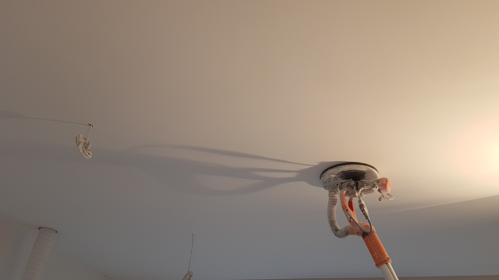 Szlifierka do gładzi gipsowych przy suficie, widoczne przewody elektryczne w tle.