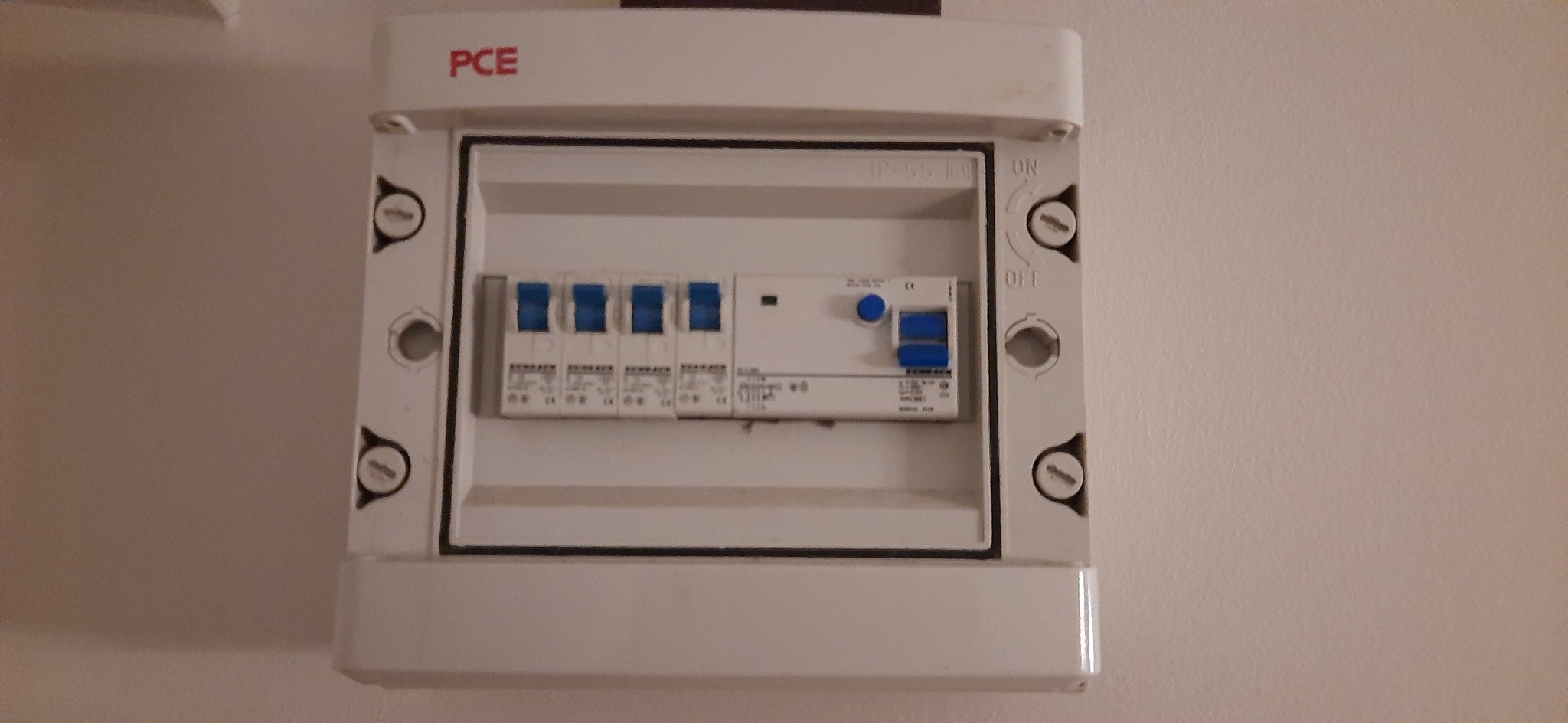 Tablica rozdzielcza z wyłącznikami nadprądowymi w obudowie PCE, widoczne śruby mocujące obudowę do ściany.