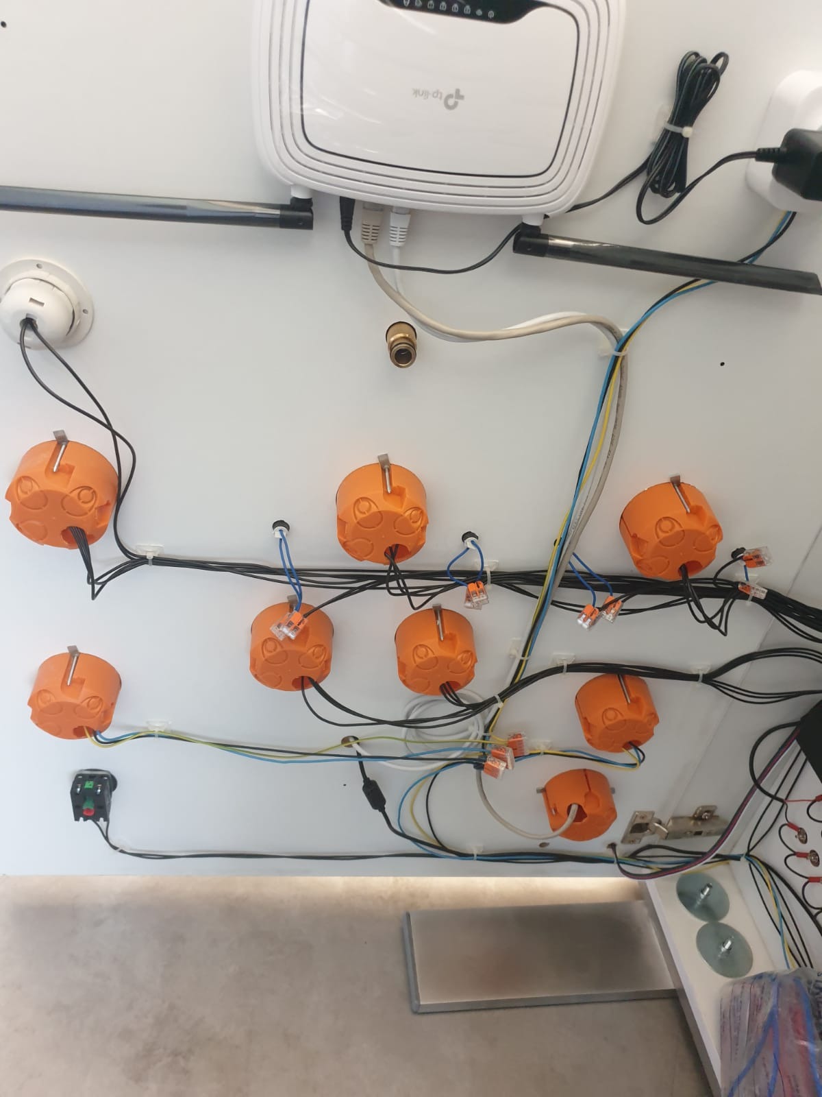 Widok od dołu na montaż instalacji elektrycznej z wykorzystaniem pomarańczowych puszek instalacyjnych i złączek Wago, widoczny router TP-Link i przewody różnego koloru.