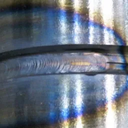 Detal spoiny obwodowej na metalowym elemencie, widoczne ślady i kolory po spawaniu.