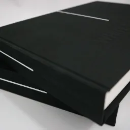 Dwa czarne, twarde oprawione albumy, jeden na drugim, z wytłoczonym napisem i białymi liniami dekoracyjnymi na okładce.