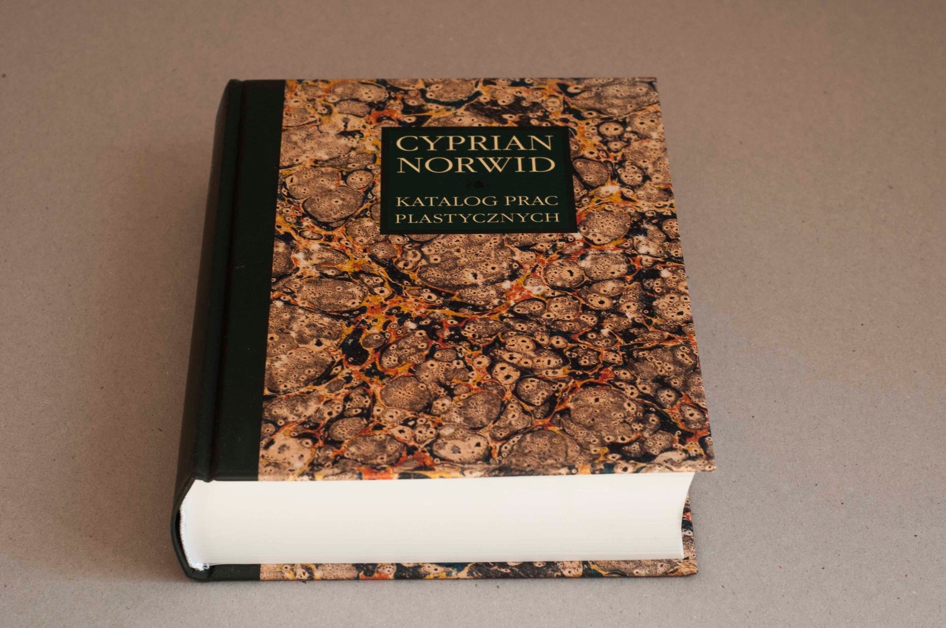 Książka Cypriana Norwida, katalog prac plastycznych, z marmurkową okładką w odcieniach brązu i czerni, oprawiona w ciemnozieloną skórę.