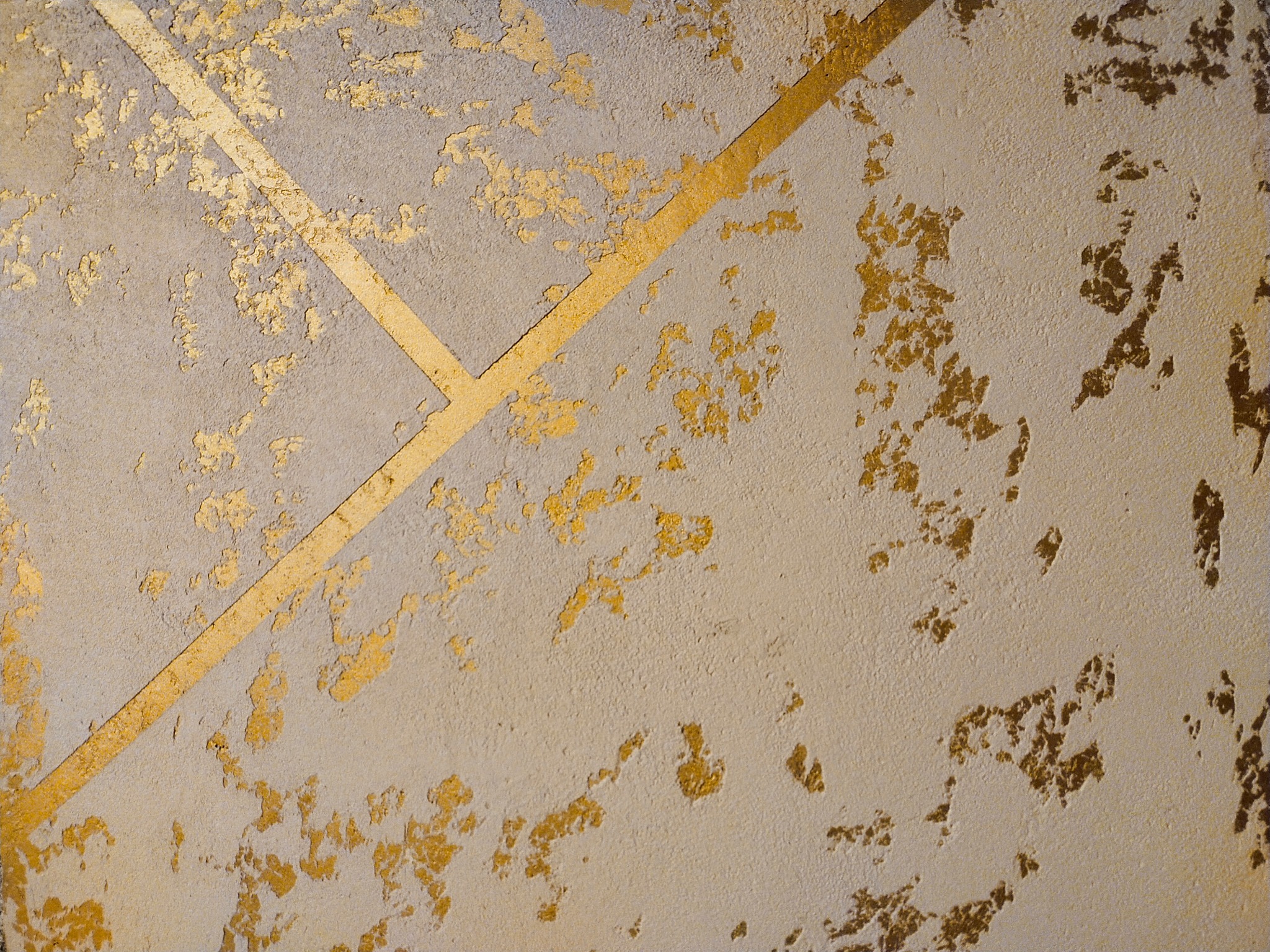 Dekoracyjna ściana z szarą fakturą i geometrycznymi złotymi paskami oraz nieregularnymi złotymi plamami, tworząca efekt postarzanego złota.