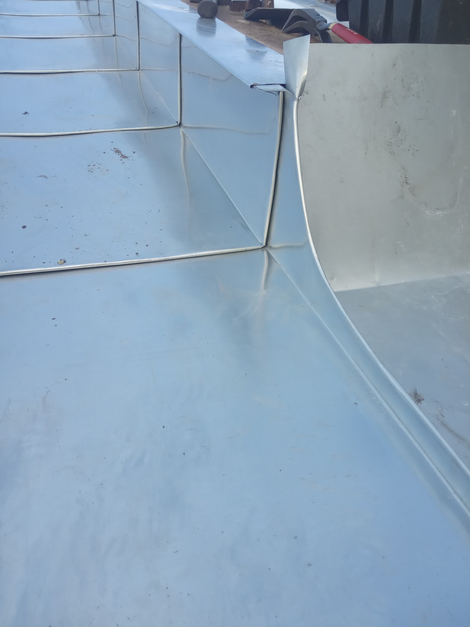 Nowe, błyszczące obróbki blacharskie na dachu z widocznymi łączeniami i fragmentem rynny, narzędzia dekarskie w tle.