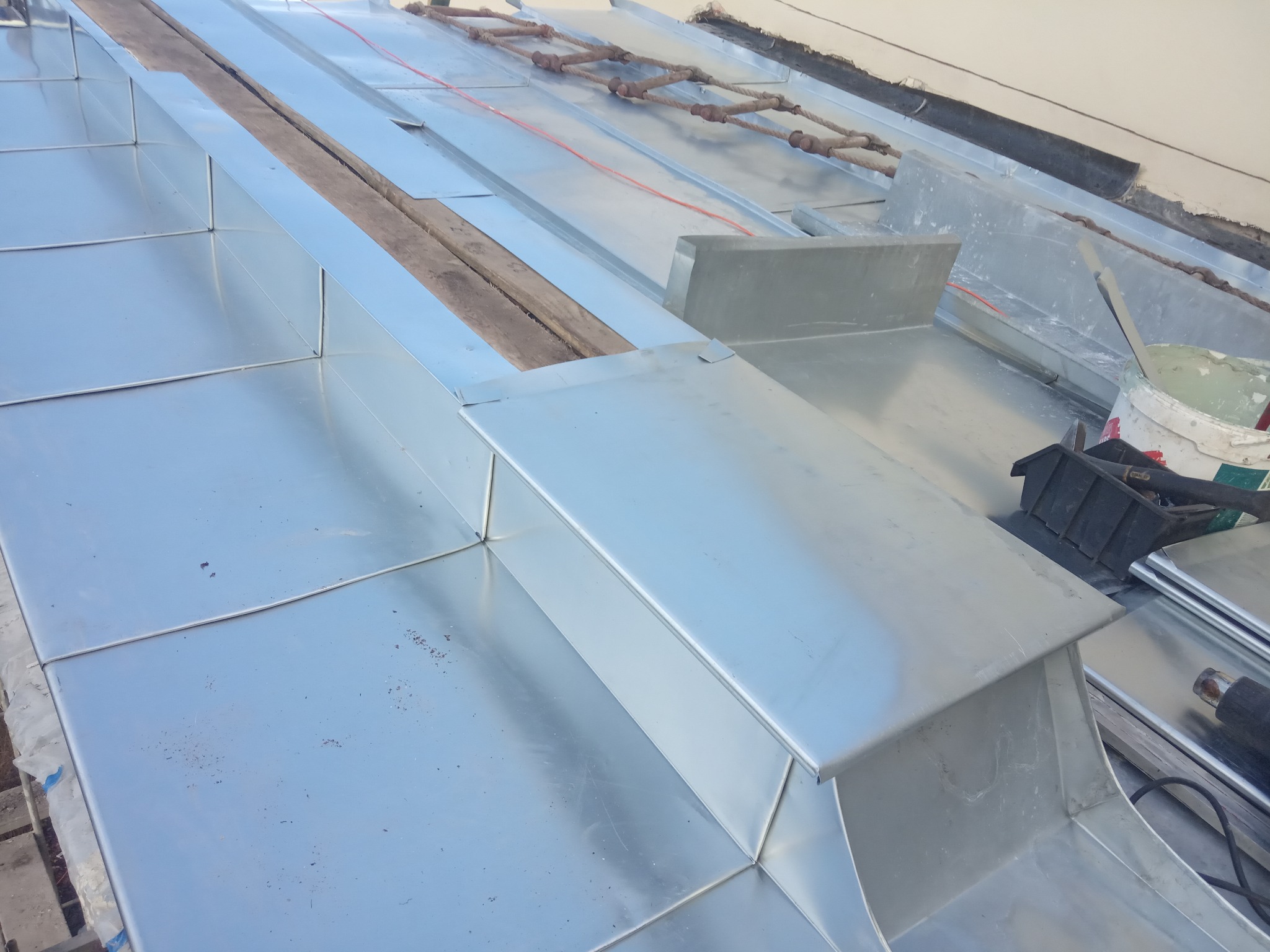 Szczegółowe ujęcie nowej, błyszczącej, metalowej konstrukcji dachu z widocznymi elementami łączeń i drewnianymi belkami konstrukcyjnymi oraz narzędziami w tle.