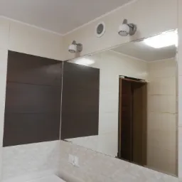 Wykończona łazienka z lustrem, brązowymi i białymi płytkami, oświetleniem punktowym i wentylacją.