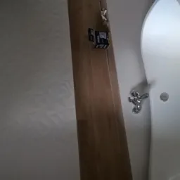 Biała wanna wolnostojąca z chromowaną baterią, częściowo widoczna na tle ściany z wzorem i drewnianej ramy drzwi z poziomnicą.