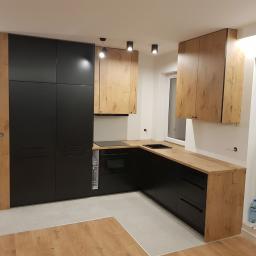 Czarno na białym - Nowoczesna kuchnia z czarnymi szafkami dolnymi i drewnopodobnymi górnymi, punktowe oświetlenie sufitowe, jasna podłoga, widok na okno.