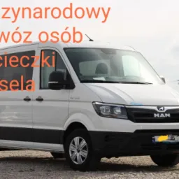 Biały bus marki MAN z przyciemnianymi szybami na parkingu, potencjalnie przeznaczony do przewozu osób, widoczne inne busy w tle.