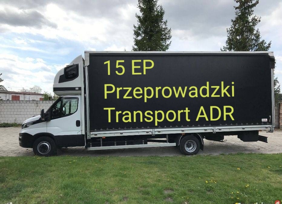 Biały samochód dostawczy z czarną plandeką, na której widnieją żółte napisy '15 EP Przeprowadzki Transport ADR', zaparkowany na trawie.