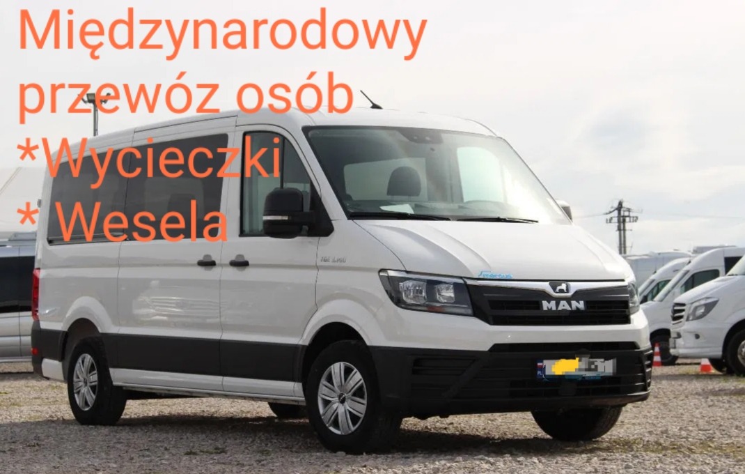 Biały bus marki MAN z przyciemnianymi szybami na parkingu, potencjalnie przeznaczony do przewozu osób, widoczne inne busy w tle.