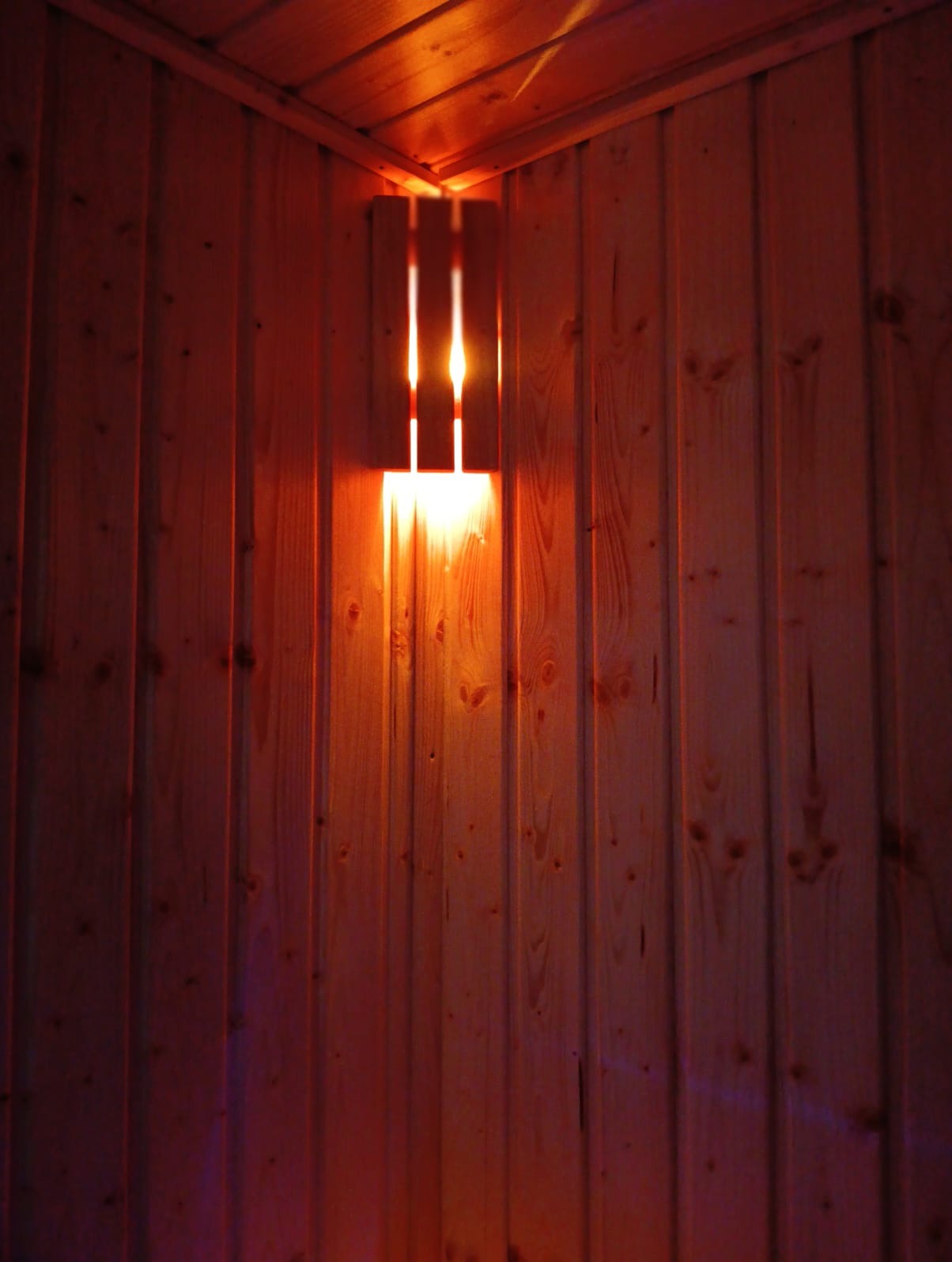 Wewnętrzna sauna fińska z oświetleniem bocznym, deski boazeryjne z widocznymi sękami, ciepłe światło lampy tworzące atmosferę relaksu.