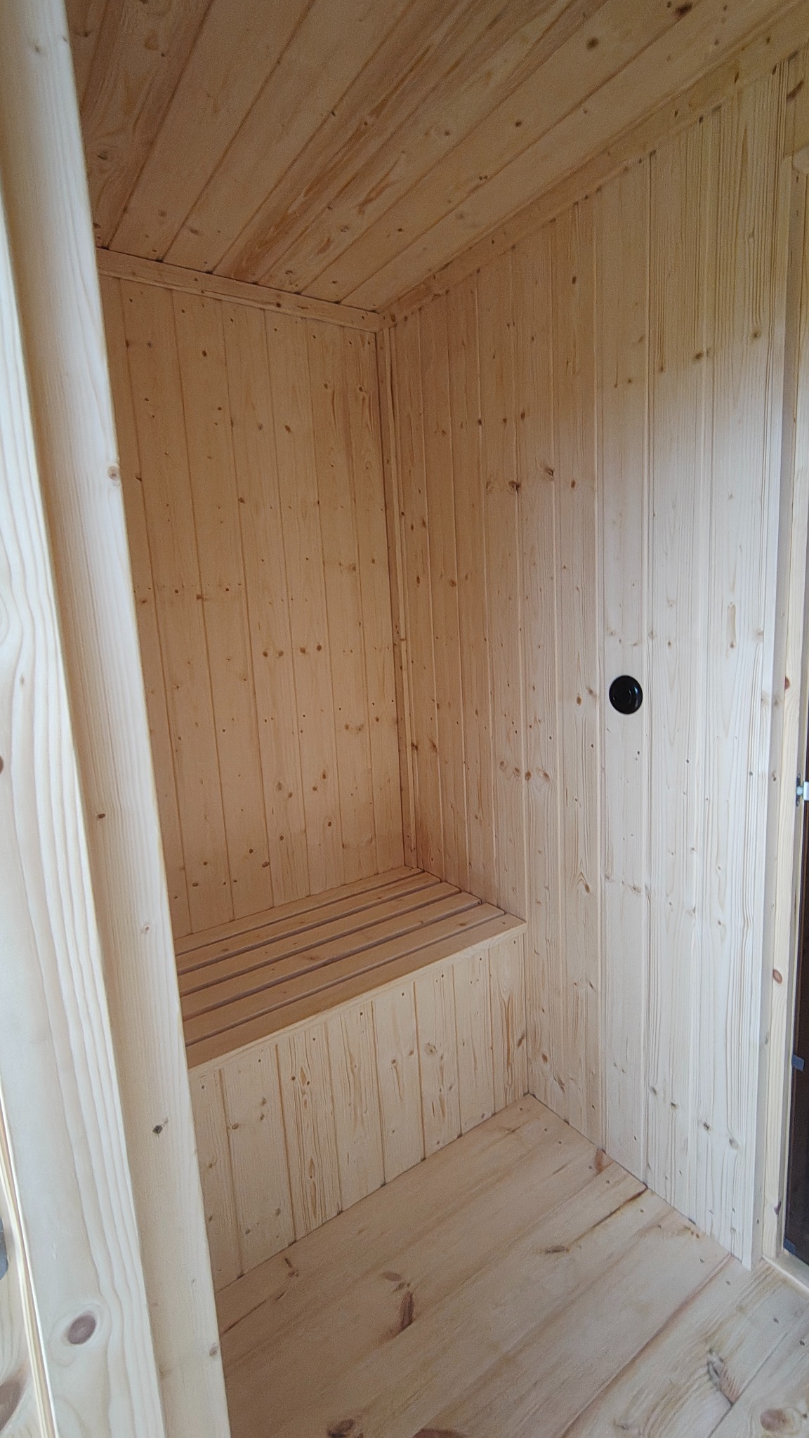 Wnętrze sauny z jasnego drewna w Żórawinie: ławka, ściany i sufit wykończone boazerią. Widoczny fragment drzwi i oświetlenie.