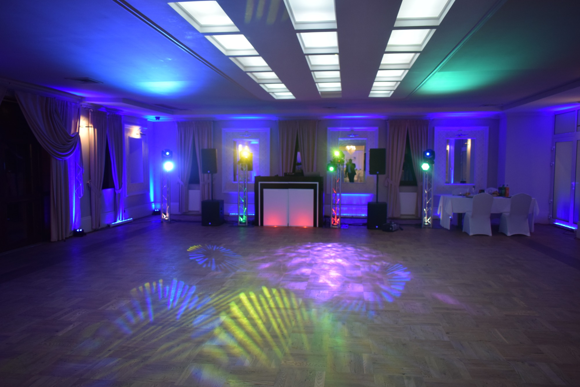 Sala bankietowa w Łodzi przygotowana na imprezę, oświetlenie dyskotekowe tworzy wzory na parkiecie, widoczny sprzęt nagłośnieniowy i stanowisko DJ-a.