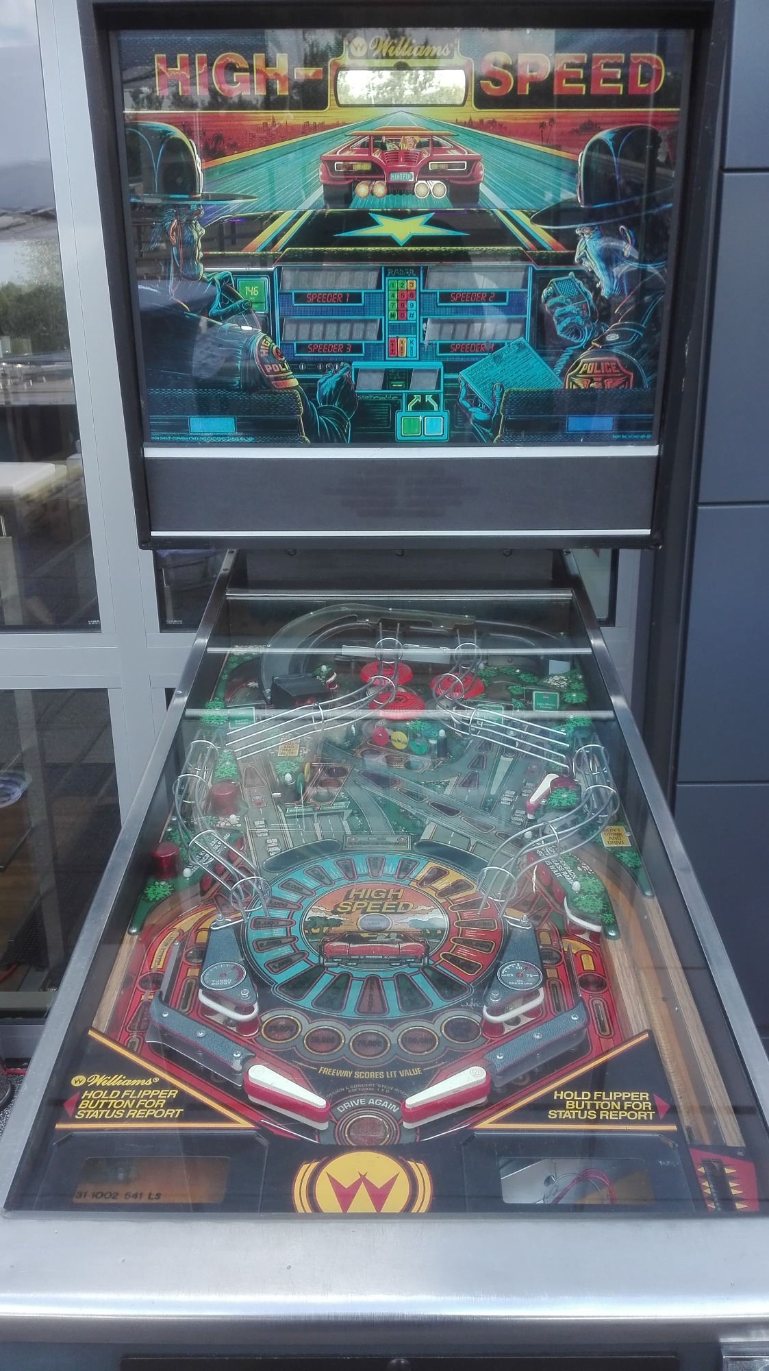 Automat do gry pinball z motywem HIGH SPEED, wyświetlający grafikę pościgu policyjnego za czerwonym samochodem sportowym na autostradzie. Widoczne flippery i elementy toru z przeszkodami.