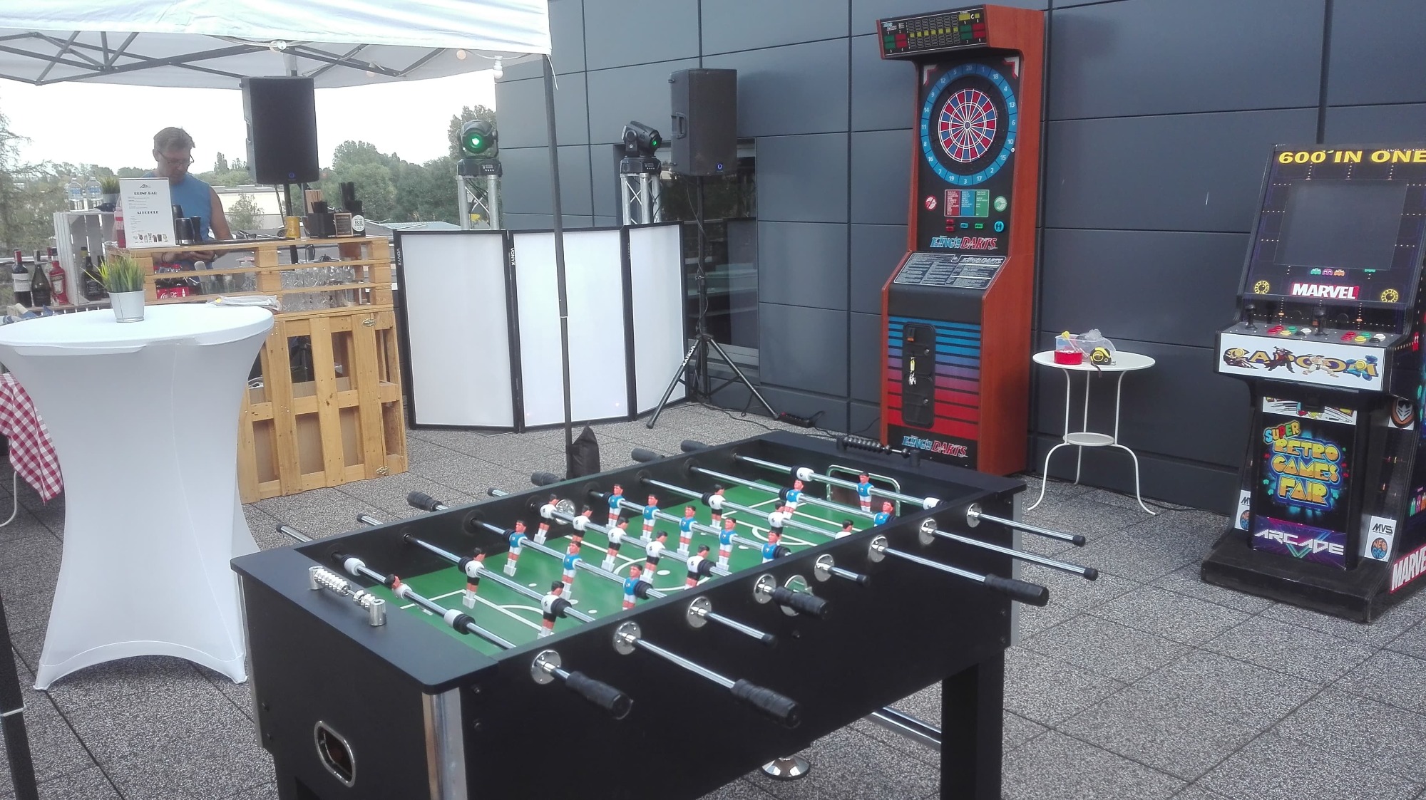 Plenerowa strefa rozrywki z piłkarzykami, automatem do gry w darta, automatem arcade z motywami Marvela, stołem barowym z obsługą i nagłośnieniem, przygotowana na imprezę.