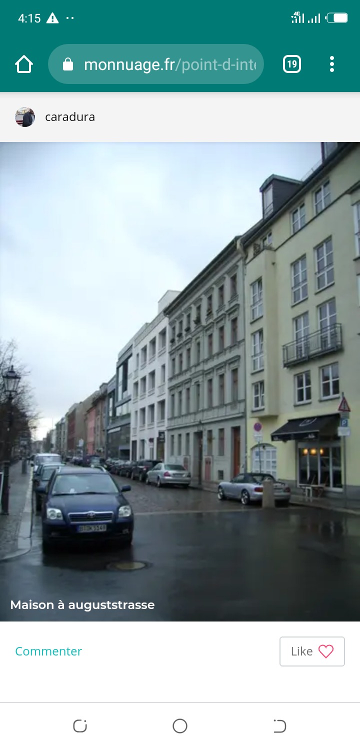 Ulica miejska w pochmurny dzień, z rzędem zaparkowanych samochodów i budynkami o różnej architekturze po obu stronach jezdni. Widoczny szyld nad wejściem do lokalu.