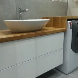 Nowoczesna łazienka w Tarnowie: biała szafka pod umywalkę z drewnianym blatem i nablatową umywalką obok pralki.