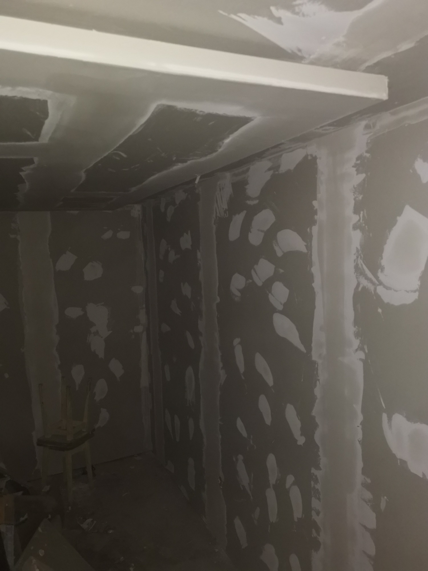 Wnętrze w trakcie prac przygotowawczych do wykończenia: ściany i sufit pokryte gładzią szpachlową, widoczne łączenia płyt gipsowo-kartonowych, listwa dekoracyjna pod sufitem.