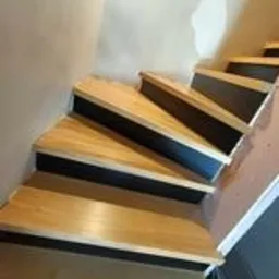 Schody drewniane z czarnymi podstopnicami, widok z dołu, podczas montażu w domu w Wejherowie. Na ścianie widoczne ślady po pracach wykończeniowych.