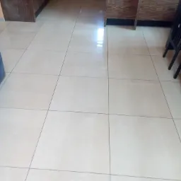 Jasne płytki podłogowe w kuchni z ciemnymi szafkami, widoczne fugi i odbicie światła na powierzchni.