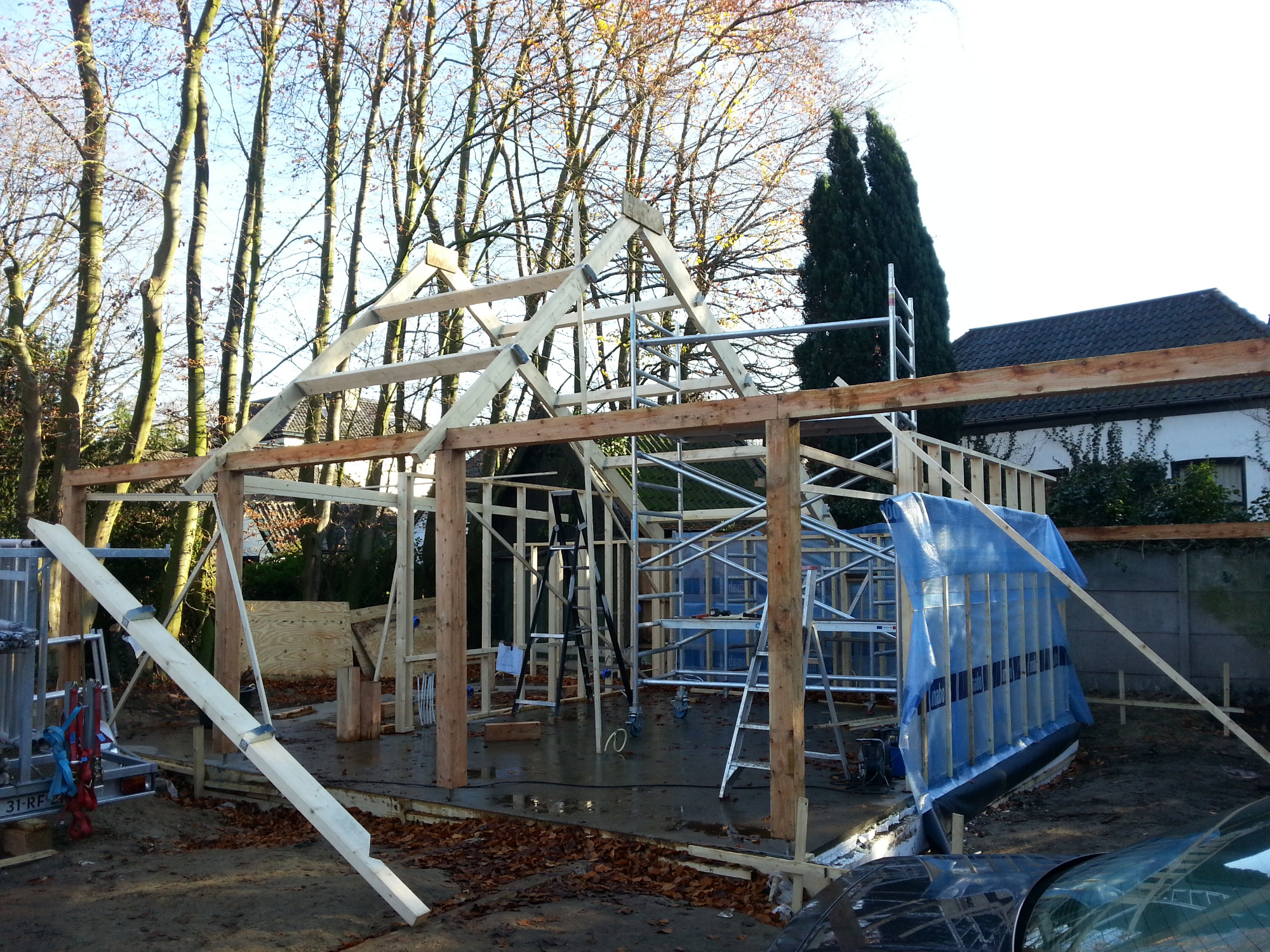 Konstrukcja szkieletowa z drewna, prawdopodobnie zadaszenia na samochody, w trakcie budowy, widoczne rusztowania i elementy drewniane.