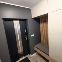 Nowoczesny przedpokój z szafą na wymiar w kolorach szarości i bieli, z siedziskiem i drewnianymi lamelami na ścianie oraz czarnymi haczykami.