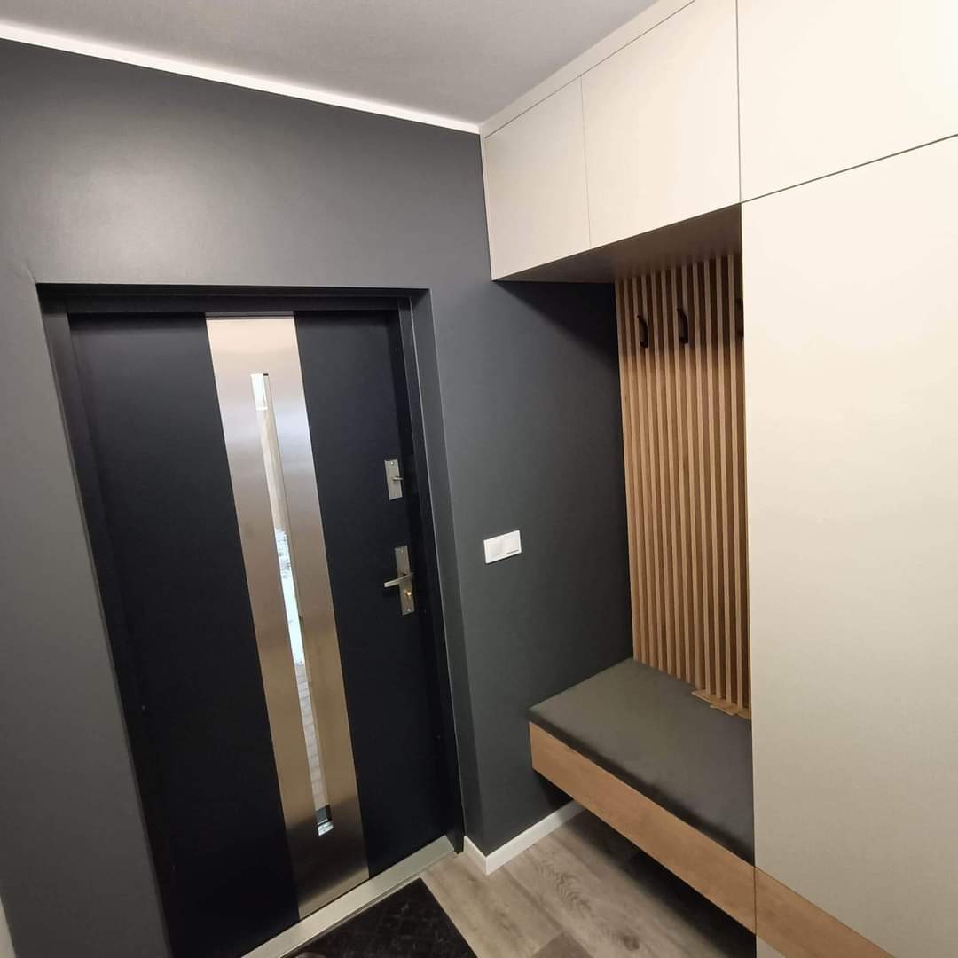 Nowoczesny przedpokój z szafą na wymiar w kolorach szarości i bieli, z siedziskiem i drewnianymi lamelami na ścianie oraz czarnymi haczykami.