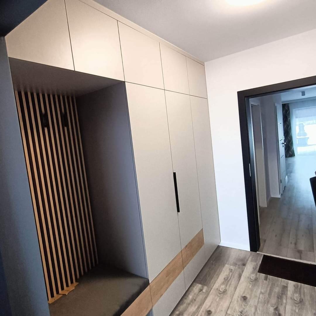 Szara szafa wnękowa z drewnianymi akcentami i siedziskiem, widok z boku, wnętrze z pionowymi listwami na ścianie, nowoczesny design.