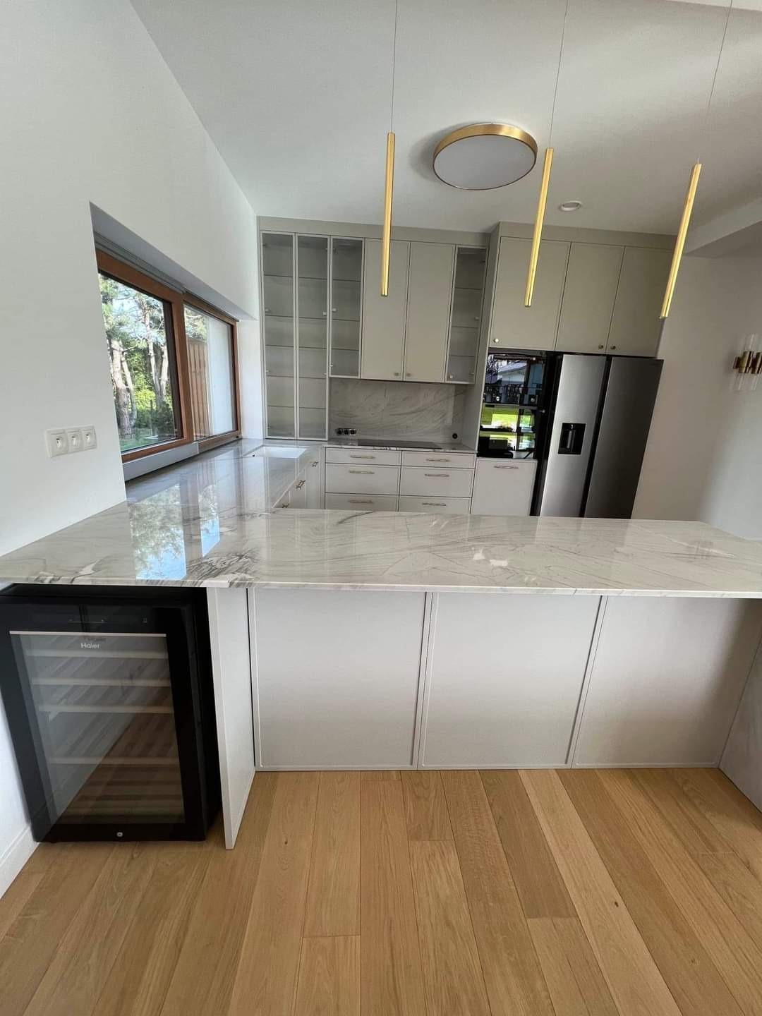 Nowoczesna kuchnia z marmurowym blatem, białymi frontami szafek i drewnianą podłogą; wbudowana chłodziarka do wina pod blatem.