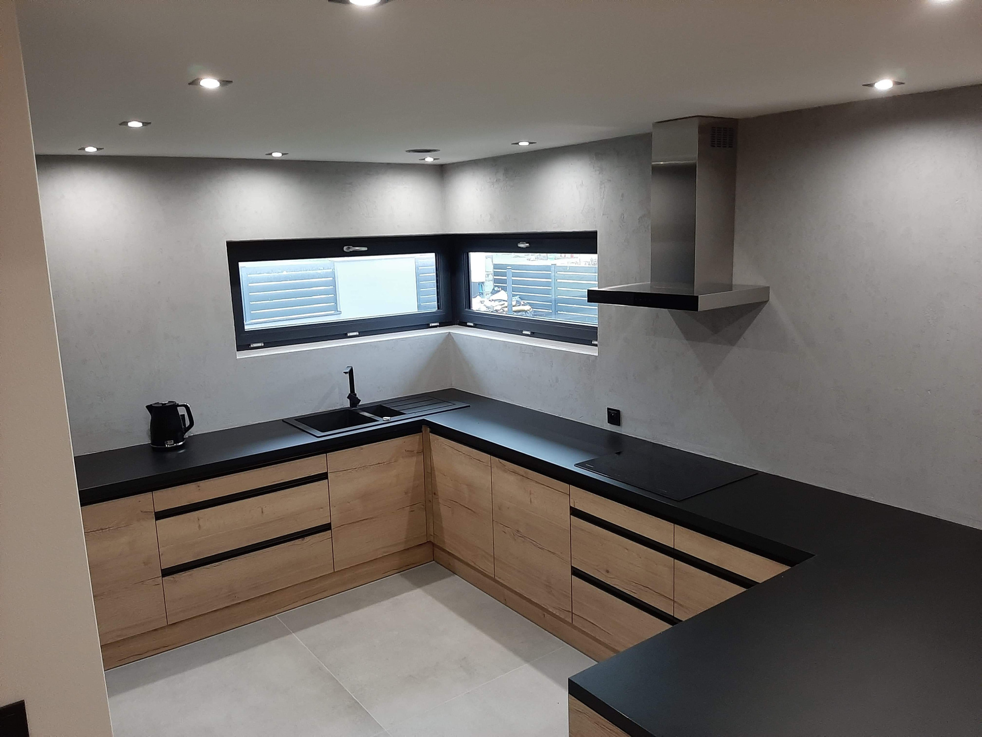 Nowoczesna kuchnia w szarościach i drewnie, z czarnym blatem i minimalistycznym oknem, oświetlenie punktowe