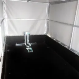 Wnętrze pustej przyczepy z czarną podłogą i jasnoszarymi ścianami oraz mocowaniem ładunku na środku.