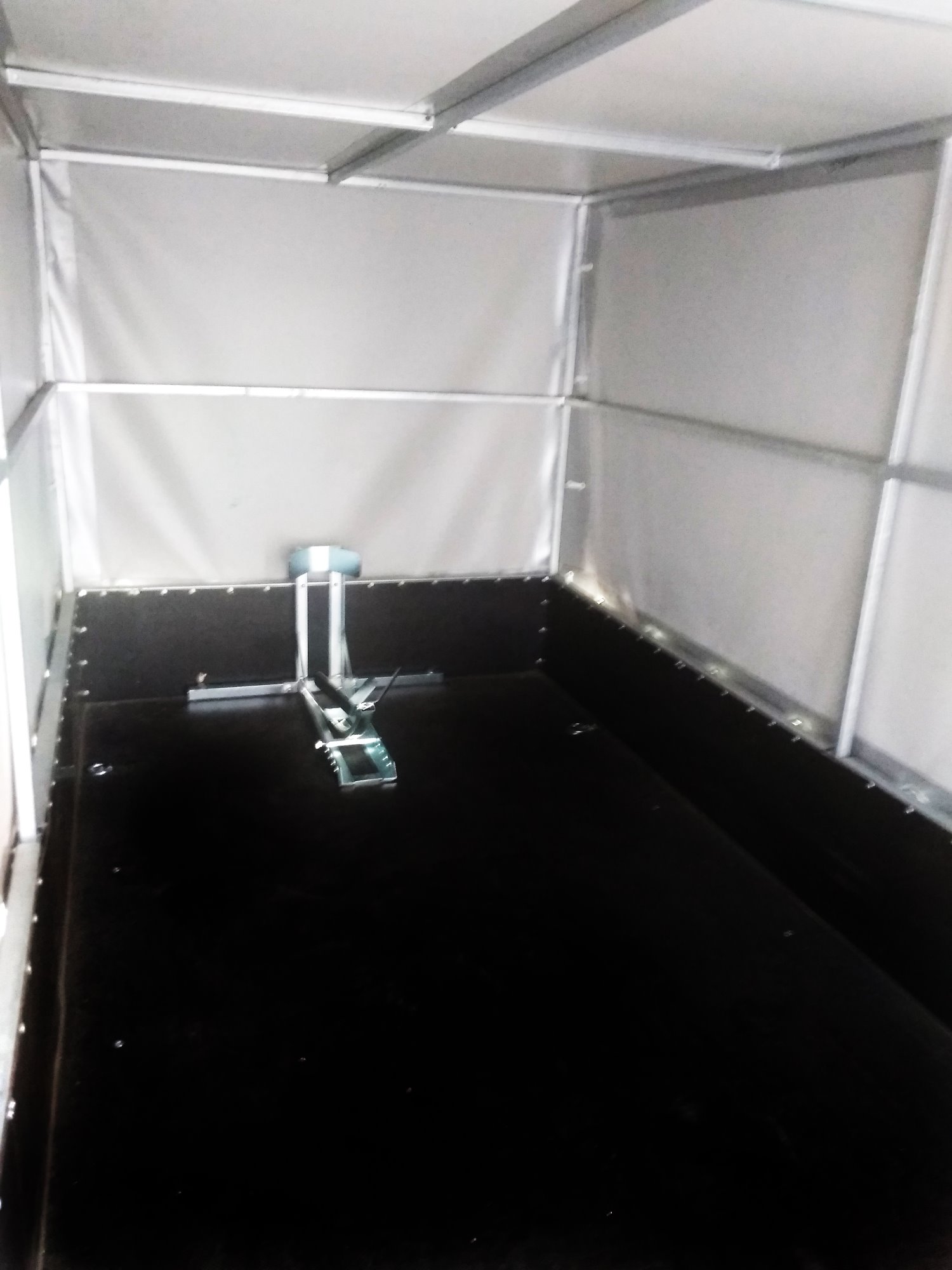 Wnętrze pustej przyczepy z czarną podłogą i jasnoszarymi ścianami oraz mocowaniem ładunku na środku.