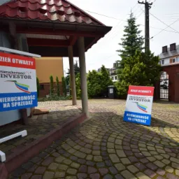 Tablice informacyjne 'Dzień Otwarty' z logo firmy 'Nieruchomości Investor' i napisem 'Nieruchomość na sprzedaż' ustawione na brukowanym chodniku przed budynkiem.