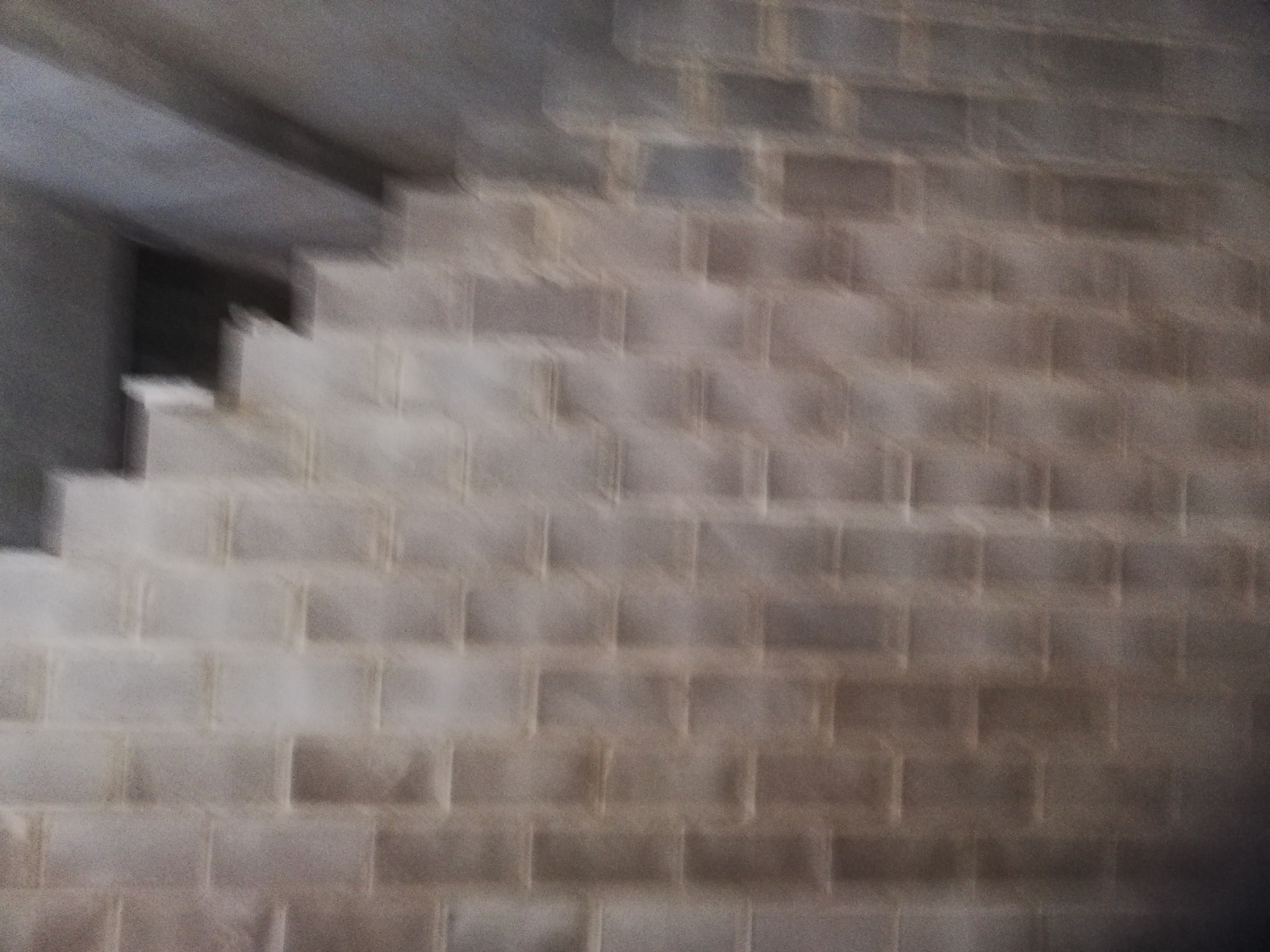 Niejasne ujęcie fragmentu murowanej ściany z bloków betonowych w Kozienicach, widoczny fragment schodów z betonu. Zdjęcie poruszone.