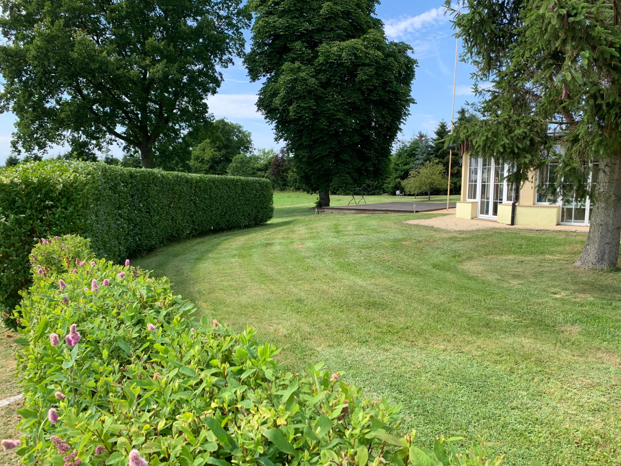 Zadbany ogród w Dziwnowie z równo przystrzyżonym trawnikiem, formowanym żywopłotem i kwitnącymi krzewami, ukazujący efekt regularnej pielęgnacji.