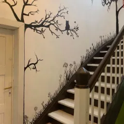 Ściana przy schodach z dekoracyjnym malunkiem przedstawiającym drzewa i kota, wykonanym czarną farbą.