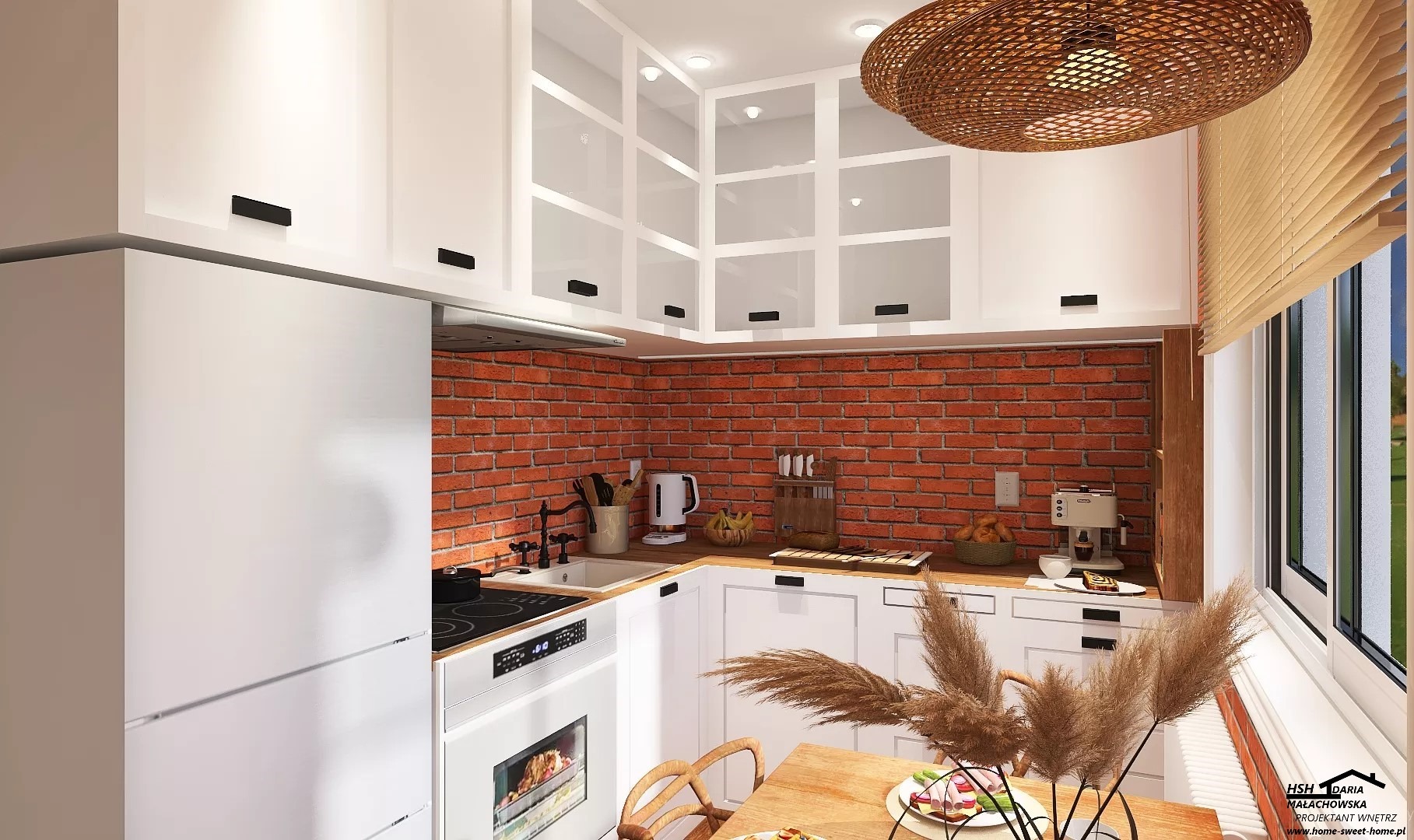 Kompaktowa kuchnia z ceglaną ścianą, białymi szafkami z czarnymi uchwytami, drewnianym blatem i okrągłą lampą z naturalnych materiałów. Na stole wazon z trawą pampasową i talerz z przekąskami.