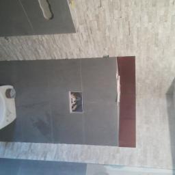 Went-Bud - Nowa toaleta podwieszana w trakcie montażu w łazience w Bytomiu, szare płytki na ścianach i podłodze, dekoracyjna ściana z małych, jasnych płytek. Widoczny otwór w ścianie na instalację.