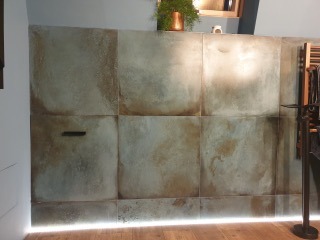 Ściana w łazience wykończona płytami imitującymi beton z widocznym oświetleniem LED u dołu i minimalistycznym uchwytem szafki.