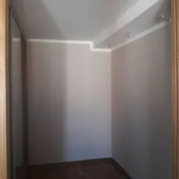 Pusty pokój z panelami podłogowymi, świeżo pomalowanymi ścianami na jasny kolor i listwami przypodłogowymi, widoczne oświetlenie sufitowe