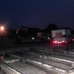Mar-Trans - Nocny widok placu budowy z ciężarówkami w tle, oświetlonego pojedynczą lampą, z formami do odlewów betonowych na pierwszym planie.