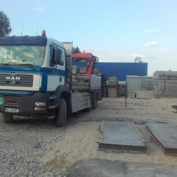 Mar-Trans - Ciężarówka MAN z czerwoną dźwignią załadowana betonowymi płytami na terenie składu budowlanego, widoczne zapasy płyt i konstrukcji betonowych.
