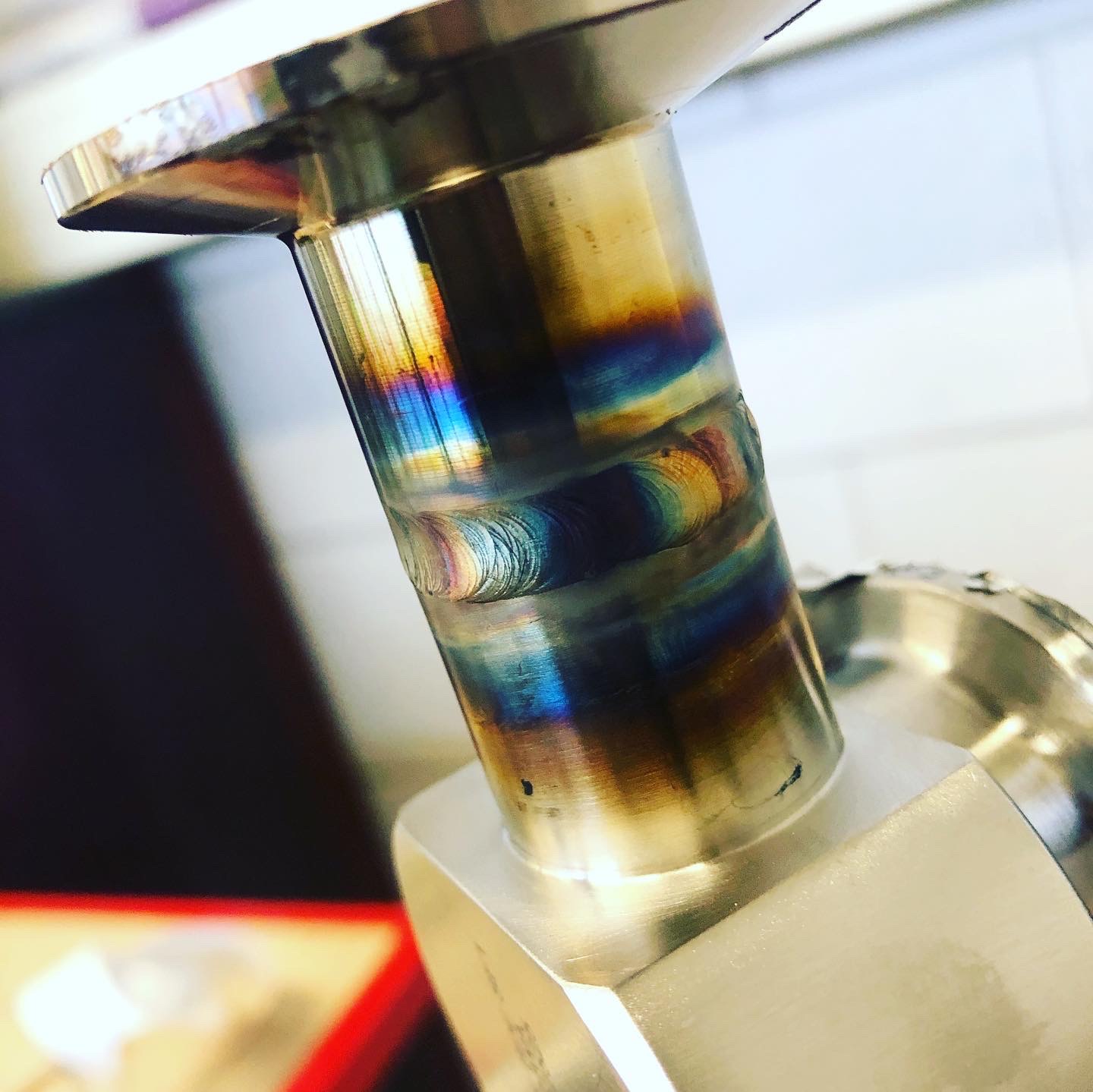 Precyzyjne spawy na metalowym elemencie, widoczne tęczowe przebarwienia termiczne, z bliska uchwycona struktura spoiny.